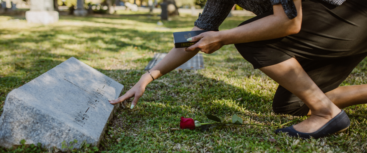 adult woman kneeling by parents grave, grieving the loss of a parent